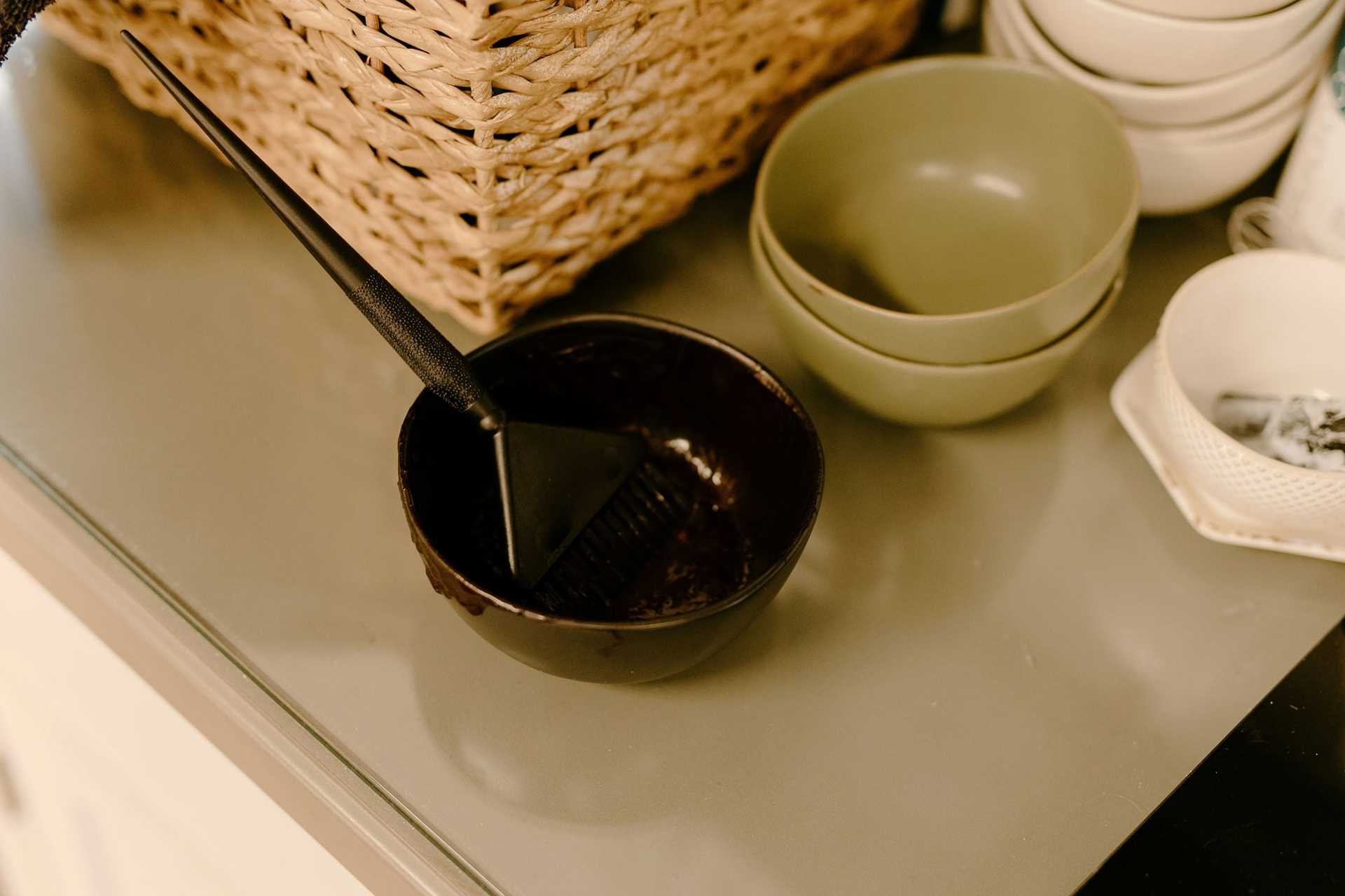 Hair dye bowl and brush on table near stack of ceramic bowls and wicker basket.